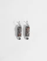 Par de aros colgantes con gancho plateado y dije cilíndrico de piedra gris con detalles marrones.