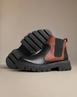Botas tipo chelsea con suela track gruesa, confeccionadas en cuero genuino. Presentan un diseño bicolor que combina paneles en negro y marrón, con elásticos laterales negros para mayor ajuste y comodidad.
