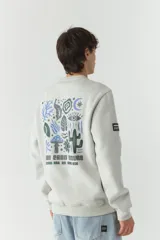 Buzo de felpa color gris claro con cuello redondo y puños y cintura acanalados. Estampado en la espalda con motivos de la naturaleza en tonos azul, verde y negro.