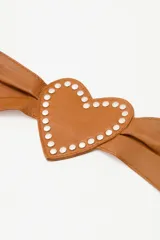 Cinturón faja de cuero ovino color suela, con diseño de hebilla en forma de corazón y detalle de tachas metálicas en todo el contorno.