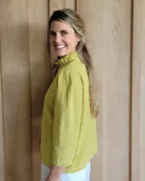 Camisa de manga tres cuartos color beige con cuello con volados y botones frontales. Presenta un detalle de color negro en la parte superior de las mangas.