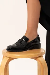 Mocasín de cuero charol negro con diseño enrejillado en la capellada, horma cuadrada y taco bajo.
