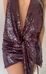 Minivestido de fiesta color borgoña con lentejuelas, escote halter pronunciado y choker al cuello. Diseño drapeado con nudo en la cintura y espalda descubierta.