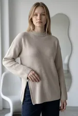 Sweater de punto acanalado en color beige, con cuello redondo y cierre metálico lateral que permite regular la apertura del ruedo. Diseño de corte holgado y mangas largas.