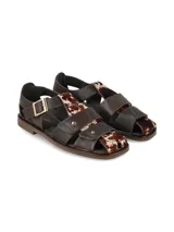 Sandalias de cuero marrón con diseño tipo franciscanas, combinadas con apliques de pelo con estampado animal print tipo vaca, hebilla metálica dorada de ajuste en el tobillo y suela plana.