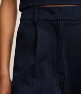 Pantalón recto de cintura baja, confeccionado en punto roma con rayas verticales en hilo teñido. Presenta trabillas en la cintura, cierre tradicional, pliegues, bolsillos cargo laterales y bolsillos falsos atrás.