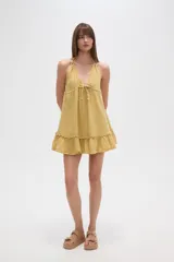 Vestido mini blanco de algodón, con escote en V, tirantes finos que se anudan en el cuello, ajuste con cordón en la cintura y volados en el ruedo.