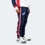 Pantalón de jogging azul marino de felpa, con franjas laterales en rojo y blanco. Presenta el escudo del Club Nacional de Football en el muslo derecho y el logo de Umbro en el izquierdo, con cintura elástica y cordón de ajuste.