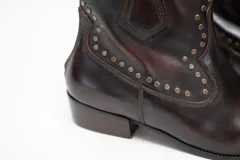Bota texana de caña baja marca Brava, confeccionada en cuero color marrón tinto con efecto envejecido. Cuenta con taco bajo, puntera fina y detalles de tachas metálicas aplicadas en los laterales y la puntera.