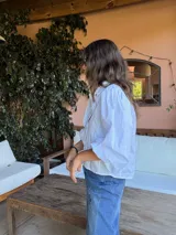 Camisa de color marrón oscuro con cuello clásico y mangas abullonadas con puños elásticos. Presenta un corte holgado y cierre frontal con botones.