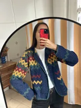 Saco tejido a mano en crochet con diseño multicolor en tonos azul, amarillo, verde y bordó. Presenta cuello solapa, cierre frontal abierto y mangas largas con patrón geométrico.