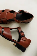 Sandalia cerrada tipo pescador, color blanco o hueso brillante, con tiras entrecruzadas en el empeine y cierre de hebilla ajustable en el lateral. Posee suela y taco bajo de color negro.