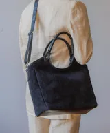 Bolso tipo shopper de gamuza color negro, forrado en su interior. Cuenta con asas de mano y una correa larga desmontable para llevar al hombro o cruzado.