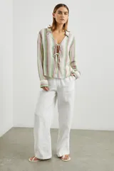 Blusa de lino a rayas verticales de color blanco, naranja, verde y marrón, con cuello camisero, mangas largas con puños y lazos ajustables en el escote.