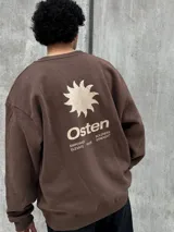 Buzo marrón con logo "Osten" y diseño gráfico de sol en color beige. Corte oversize, cuello redondo y mangas largas.