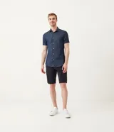 Camisa azul de manga corta con cuello clásico, corte slim fit, cierre frontal con botones blancos y bolsillo de parche en el pecho.