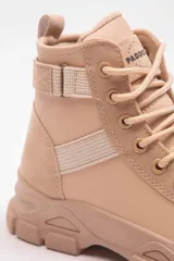 Bota militar beige con cordones, suela gruesa track y detalles de tiras elásticas en el lateral.