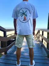 Remera oversize de color beige con estampa en la espalda de una palmera y una tabla de surf, acompañada de la inscripción "Surfer's Paradise Laguna Beach".