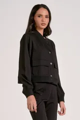 Camperita tipo bomber color beige claro, con cuello redondo acanalado, cierre frontal con broches metálicos y bolsillos delanteros con tapa. Los puños y el bajo son acanalados.