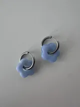 Aros de acero quirúrgico tipo argolla con dije colgante en forma de flor de color celeste.
