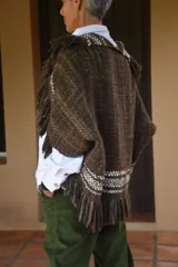 Capita artesanal de lana merino pura, color marrón con textura tejida y flecos decorativos en los bordes.