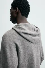 Jersey de lana gris, corte regular, con cuello pico que incorpora una capucha y manga larga. Presenta acabados en rib en puños y bajo.