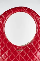 Cartera acolchada negra de silueta ovalada con asa circular integrada y diseño matelassé en rombos.