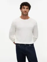 Sweater de punto liso en color blanco marfil, con cuello redondo, mangas largas y puños y dobladillo acanalados.