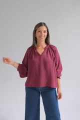 Blusa bordó de corte holgado, con escote en V y cuello fruncido. Presenta mangas tres cuartos con puños elásticos y detalles de volados.