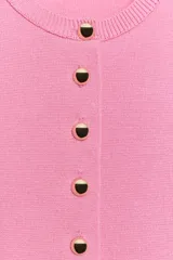Chaqueta de punto de manga corta en color rosado, con cuello redondo y cierre frontal de botones dorados.
