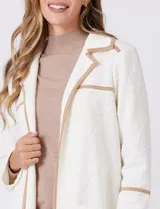 Chaqueta de silueta estructurada y calce recto, confeccionada en tejido jacquard con relieve floral. Presenta cuello con solapas, frente abierto y dos bolsillos de parche frontales. Se destaca por sus vivos a contratono que bordean las solapas, los bolsillos y las costuras horizontales, además de contar con tajos laterales en el ruedo.