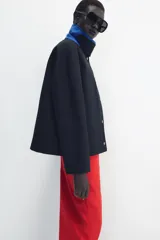 Chaqueta de Zara Woman Collection color negro, de cuello con solapa y manga larga. Cuenta con bolsillos delanteros ocultos en las costuras, cierre frontal con botones metálicos a presión y detalle de diseño asimétrico en azul en el cuello.