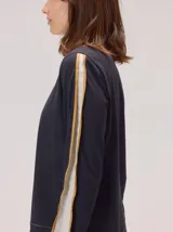 Remera de manga larga color gris claro, con detalle de franjas laterales en contraste color amarillo en las mangas. Presenta un diseño holgado y moderno.