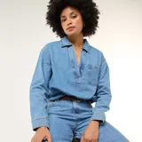 Camisa de jean de manga larga en tono azul medio, con cuello camisero, escote en V profundo y un bolsillo aplicado en el pecho.