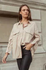 Camisa beige oversize de manga larga con cuello clásico, cierre frontal con botones y dos bolsillos con solapa en el pecho.