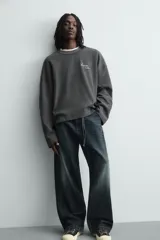Sudadera de corte relajado confeccionada en tejido de algodón con textura acanalada. Presenta cuello redondo, manga larga y un diseño con efecto lavado. Incluye un texto estampado en contraste en la parte frontal.