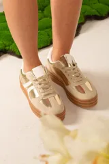 Championes urbanos color dorado y beige con detalles en blanco y suela marrón.