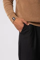 Sweater de tejido de punto grueso color tostado, con cuello redondo y mangas largas con puño elástico que incluye una etiqueta decorativa.