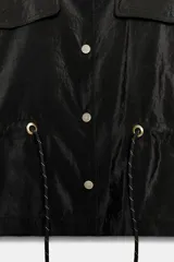Cazadora satinada de color negro, con cuello subido, bolsillos con solapa en el pecho y cordón ajustable en la cintura. Cierre frontal con botones metálicos y mangas anchas.
