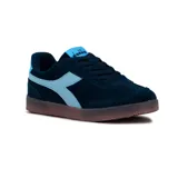 Championes urbanos Diadora modelo Bamtelo para mujer, confeccionados en gamuza color azul marino con detalles en celeste claro en los laterales, lengüeta y talón. Cuenta con suela translúcida de goma y cordones al tono.
