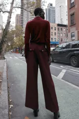 Pantalón de tiro alto color bordó, con pinzas delanteras, bolsillos frontales y falsos bolsillos con solapa en la espalda. Tiene pernera ancha y cierre frontal con cremallera, botón interior y gancho.