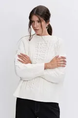 Sweater de punto color blanco off-white, con cuello redondo y diseño texturizado con trenzas y pompones en el frente.