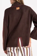 Polera de punto con calce oversize, cuello alto y mangas largas. Presenta un diseño en color negro con franjas laterales en las mangas y detalle en el cuello en tono bronce con acabado brillante.