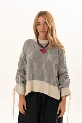 Buzo de tejido de punto con diseño geométrico en relieve, cuello redondo y mangas largas abullonadas con puños ajustables mediante lazos. Presenta un borde inferior en tejido acanalado de color crudo.