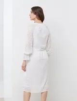 Vestido midi blanco de gasa labrada, con cuello a la base y escote en V. Cintura con lazo de ajuste, manga larga con puño elastizado y volado.