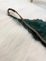 Conjunto de lencería compuesto por un bralette de encaje verde esmeralda con cierre frontal y una tanga a juego con tiras regulables, ambos con detalles de ribetes en color marrón.