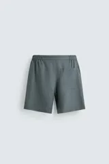 Bermuda de lino color blanco hueso, de corte relajado y tiro medio. Presenta cintura elástica ajustable con cordón, pliegues frontales y bolsillos laterales y trasero.