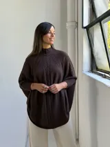 Poncho de punto color chocolate con cuello alto y diseño de trenzas verticales en el frente. Presenta mangas tres cuartos con puños acanalados y un corte holgado y fluido.