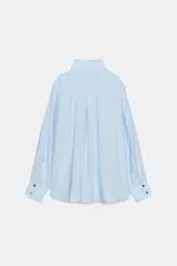 Camisa de cuello alto y manga larga, confeccionada en tejido satinado. Presenta un diseño con pliegue frontal decorativo con botón visible y cierre frontal con botones ocultos bajo solapa.