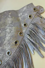 Faja de cuero marrón con detalles plateados, flecos y ojales metálicos.